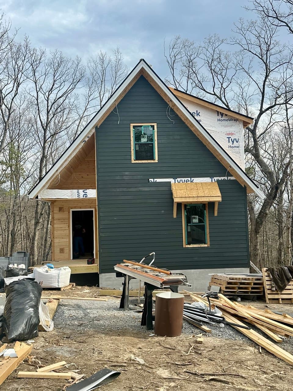 Front facade — gable peak, windows set, dark green siding