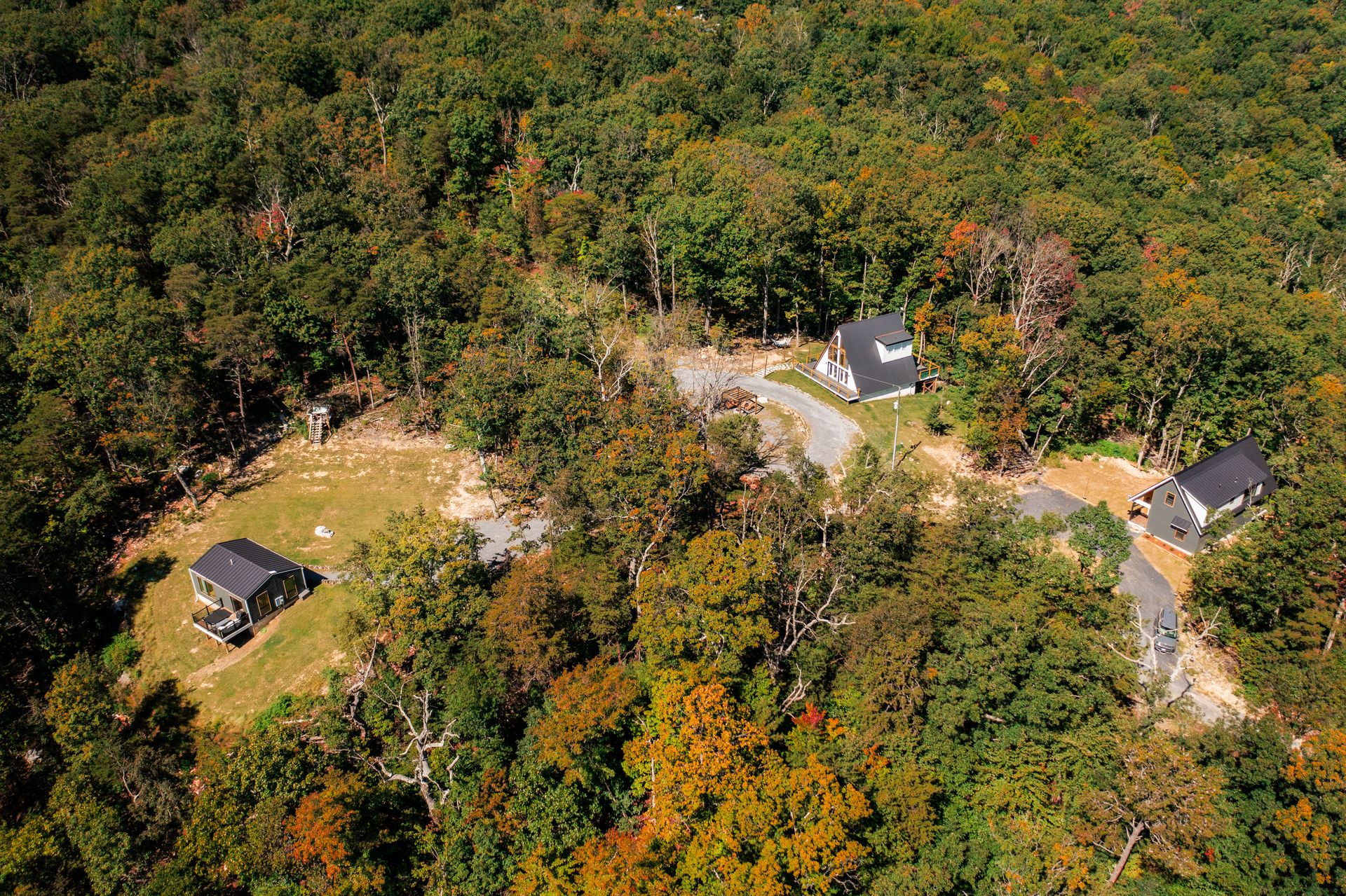 Aerial view of all three Kamara Cabins in the woods outside Luray: The Turtle on its lawn at left, The Sparrow's white A-frame in the middle and The Stag at right, linked by a gravel drive among early fall color